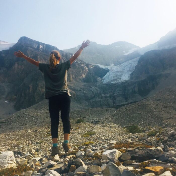 Girl standing with raised arms in front of a glacier on a hike to Stanley Glacier in British Columbia