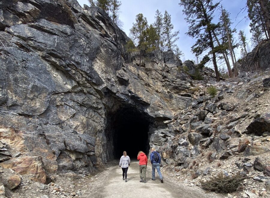 Three people about to walk into a tunnel in a rockface at the Myra Canyon Trestles.