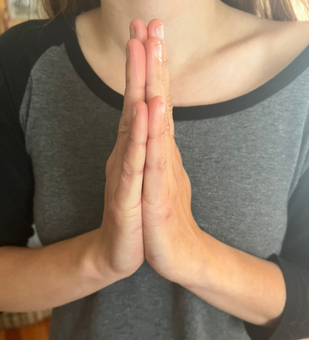 A photo of a girl's hands pressed together, fingers pointing upwards. This is the hand gesture for the greeting Namaste you should know before going to Nepal.