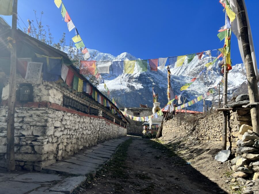 Prayer flags, stone buildings, and snowy mountains in the background in Nepal