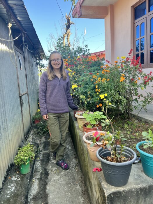 A woman standing outside surrounded by potted flowers. 