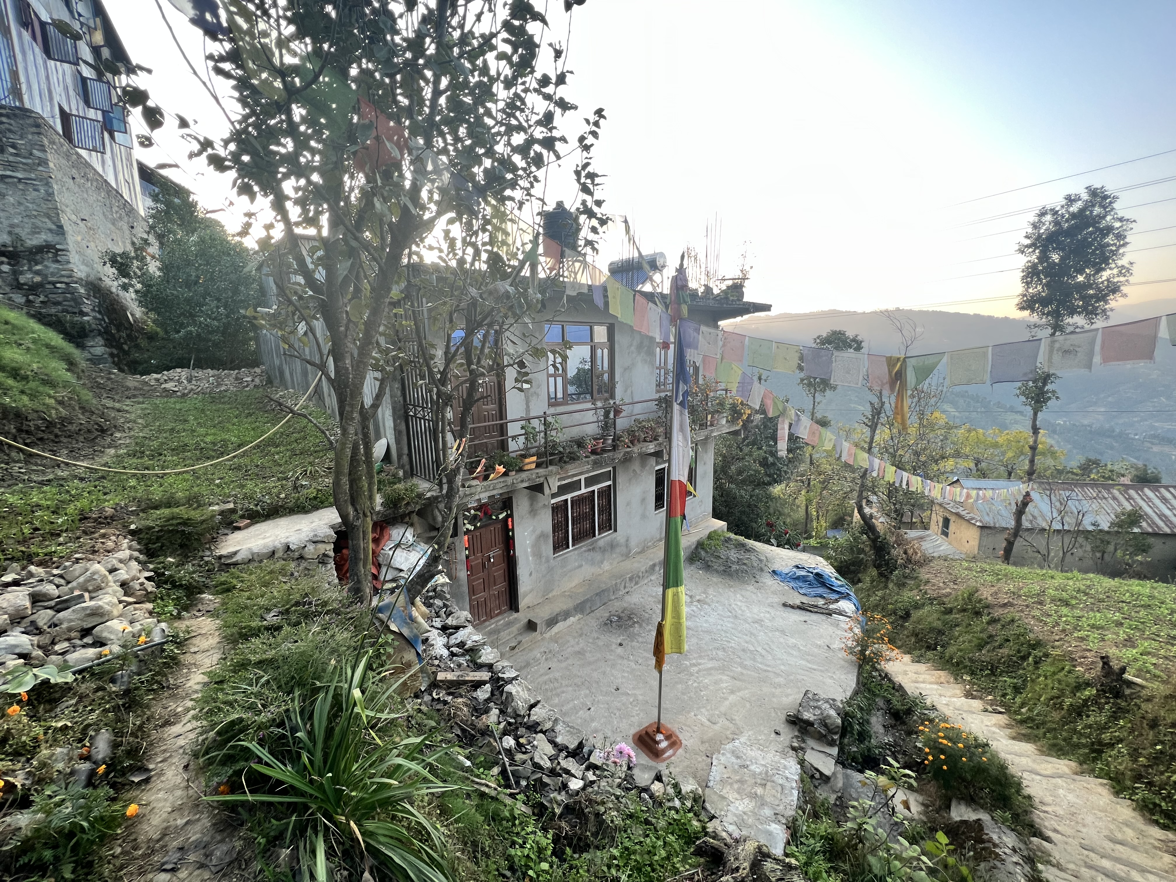 One of the homes in the Patlekhet Community Homestay Program, located on a hill surrounded by greenery and prayer flags.