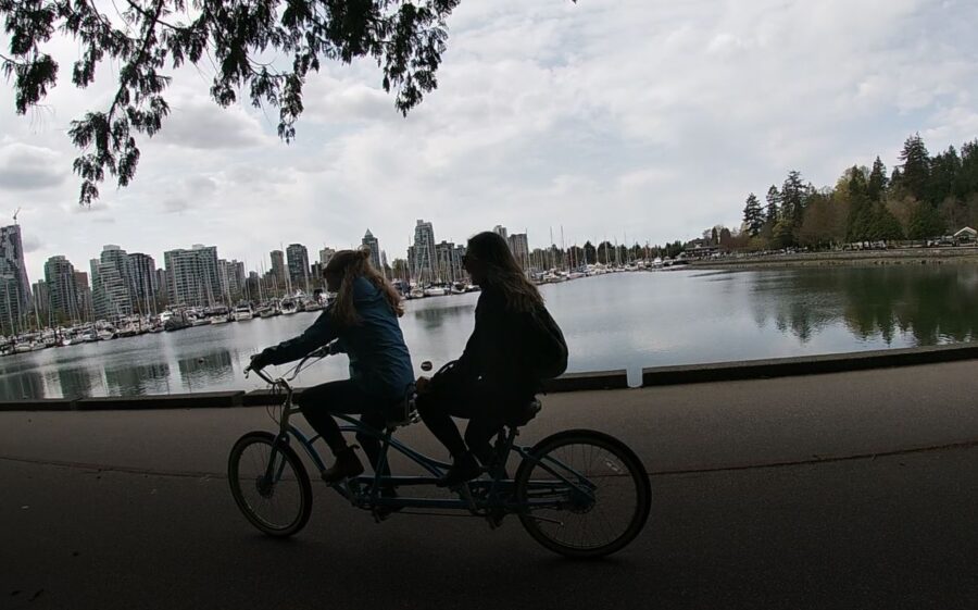 Two girls on a tandem bicycle, biking around Stanley park, as park of a BC summer road trip.