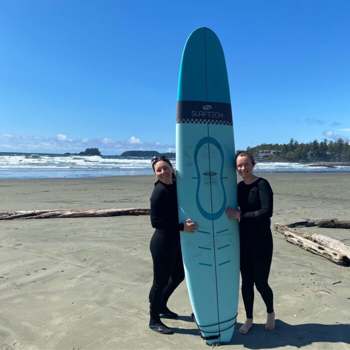 Two girls posing with a surfboard on a beach near Tofino, British Columbia. 