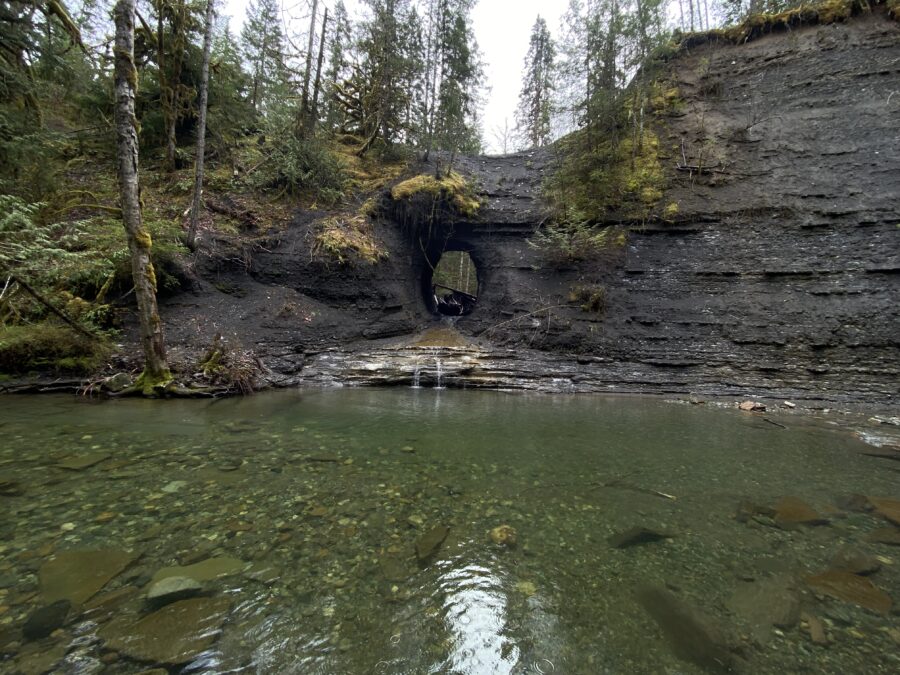 A rock face with a circular hole in it and water below, appropriately named A Hole in The Wall, near Port Alberni, BC.