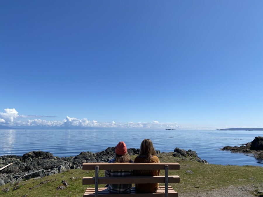 Two girls sitting on a bench overlooking the ocean, during a BC summer road trip.