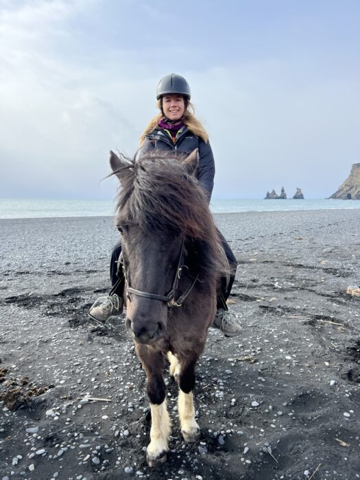 A woman riding an Icelandic horse on a black sand beach in Vik, Iceland,