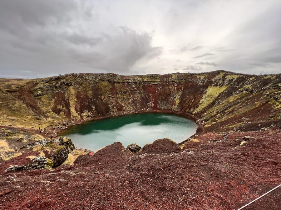 A large crater with red and mossy green around it, and water at the bottom.