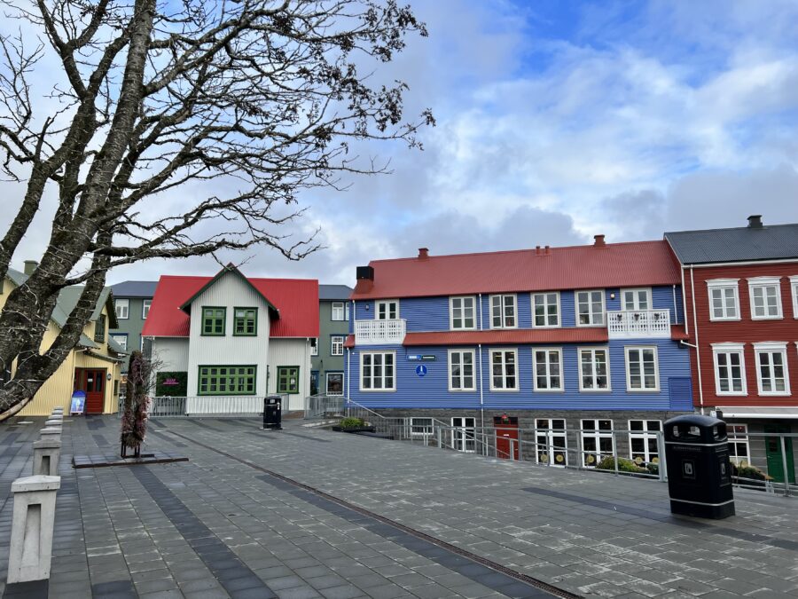 A city street with brightly coloured buidings (green, blue, red). 