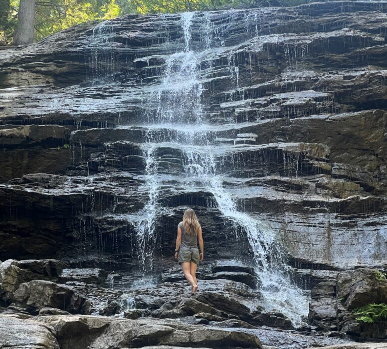 A girl standing under Moses Falls, one of the waterfalls in Revelstoke.