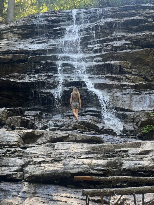 A girl standing under Moses Falls in Revelstoke. 