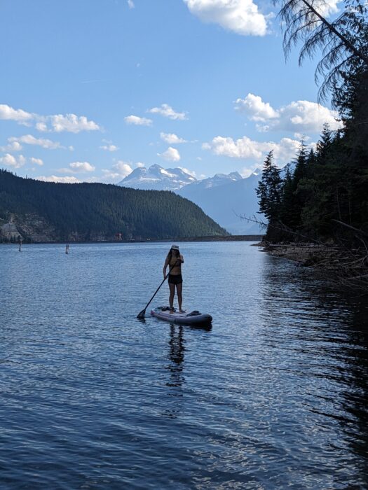 A girl paddle boarding on Lake Revelstoke with mountains in the background. 