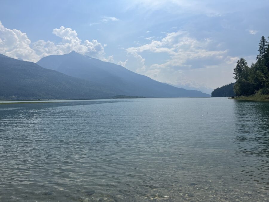 A lake in Revelstoke with mountains in the background and blue sky with clouds in it. 