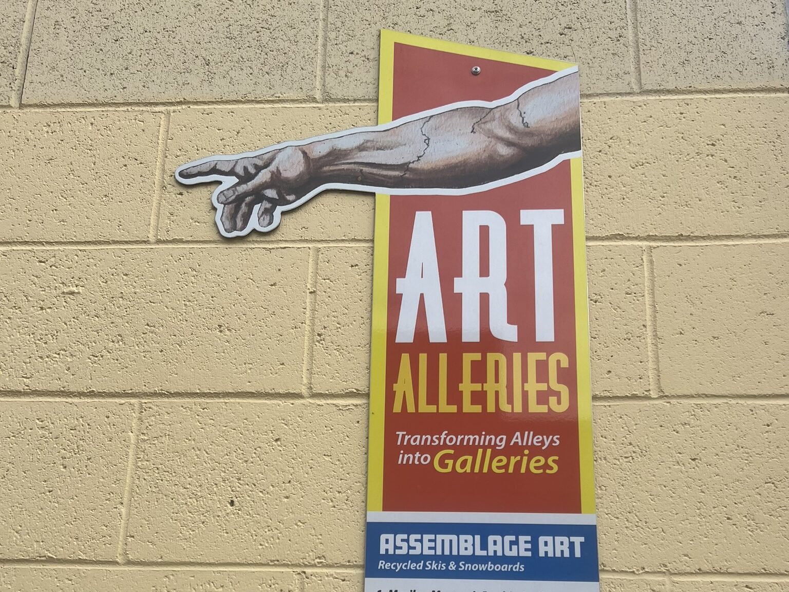 A sign with a hand pointing that says "ART ALLERIES, Transforming Alleys into Galleries"