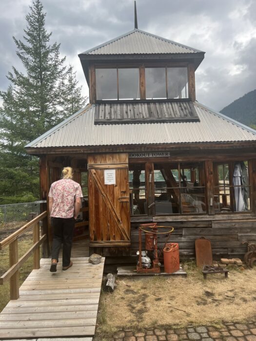 A small wooden building, an example of a fire tower, with a man walking into it