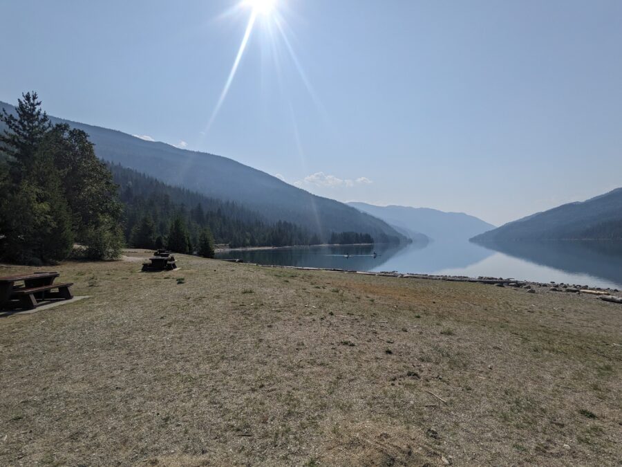 The beach at Martha Creek Provincial Park, with blue skies, mountains in the background, and a few picnic tables on the edge of the photo