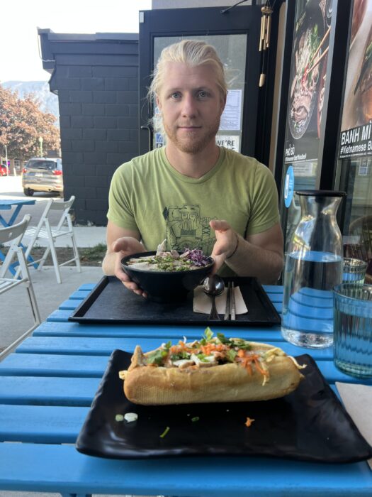 A man sitting at Sincero Cafe with a Pho soup and Banh Mi sandwich on the table