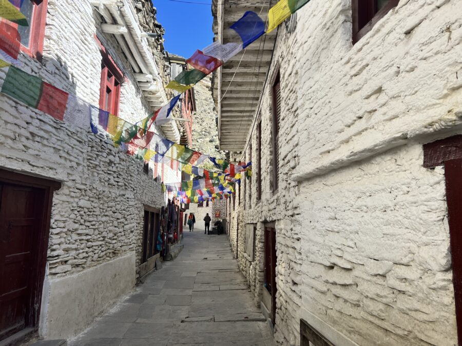 A stone street closely lined with white stone buildings and colourful prayer flags overhead in Marpha, Nepal