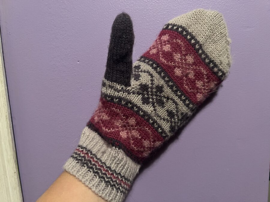 A pink, white, and grey wool mitten with an Icelandic design