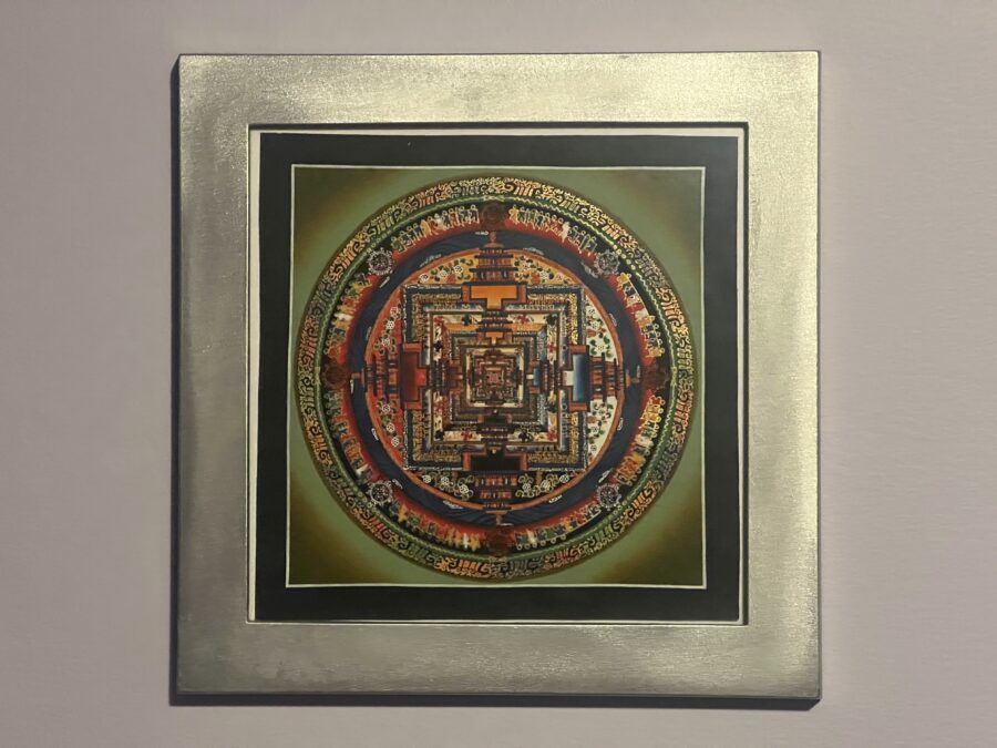 A framed Thangka painting of a mandala hanging on a wall