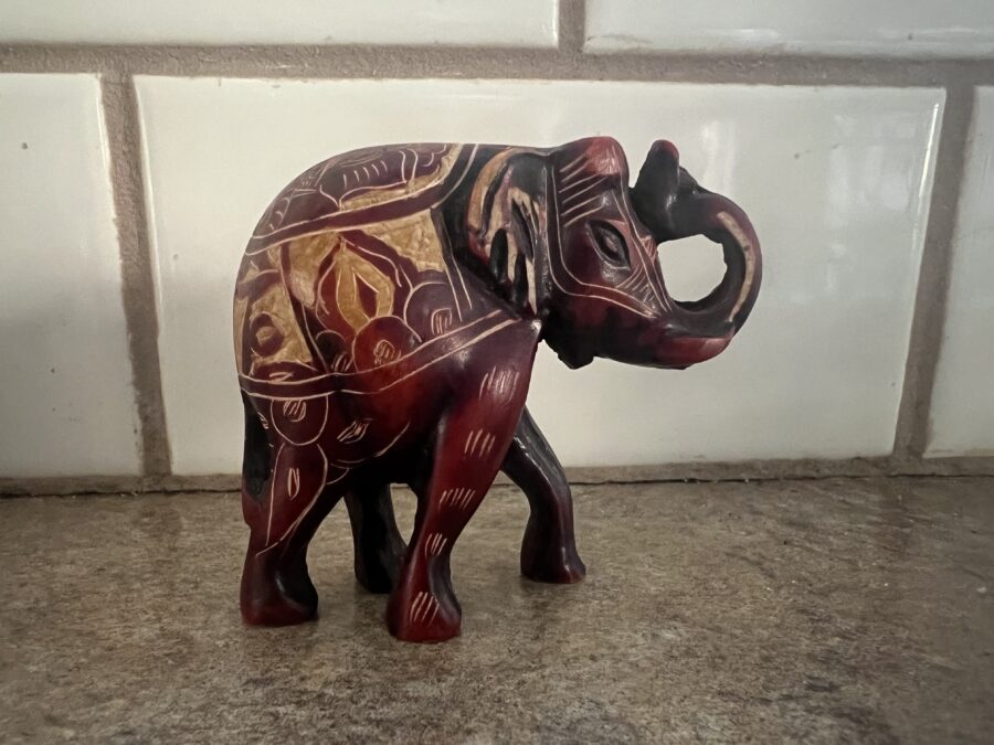 A red, wooden, elephant with different symbols and designs carved into it