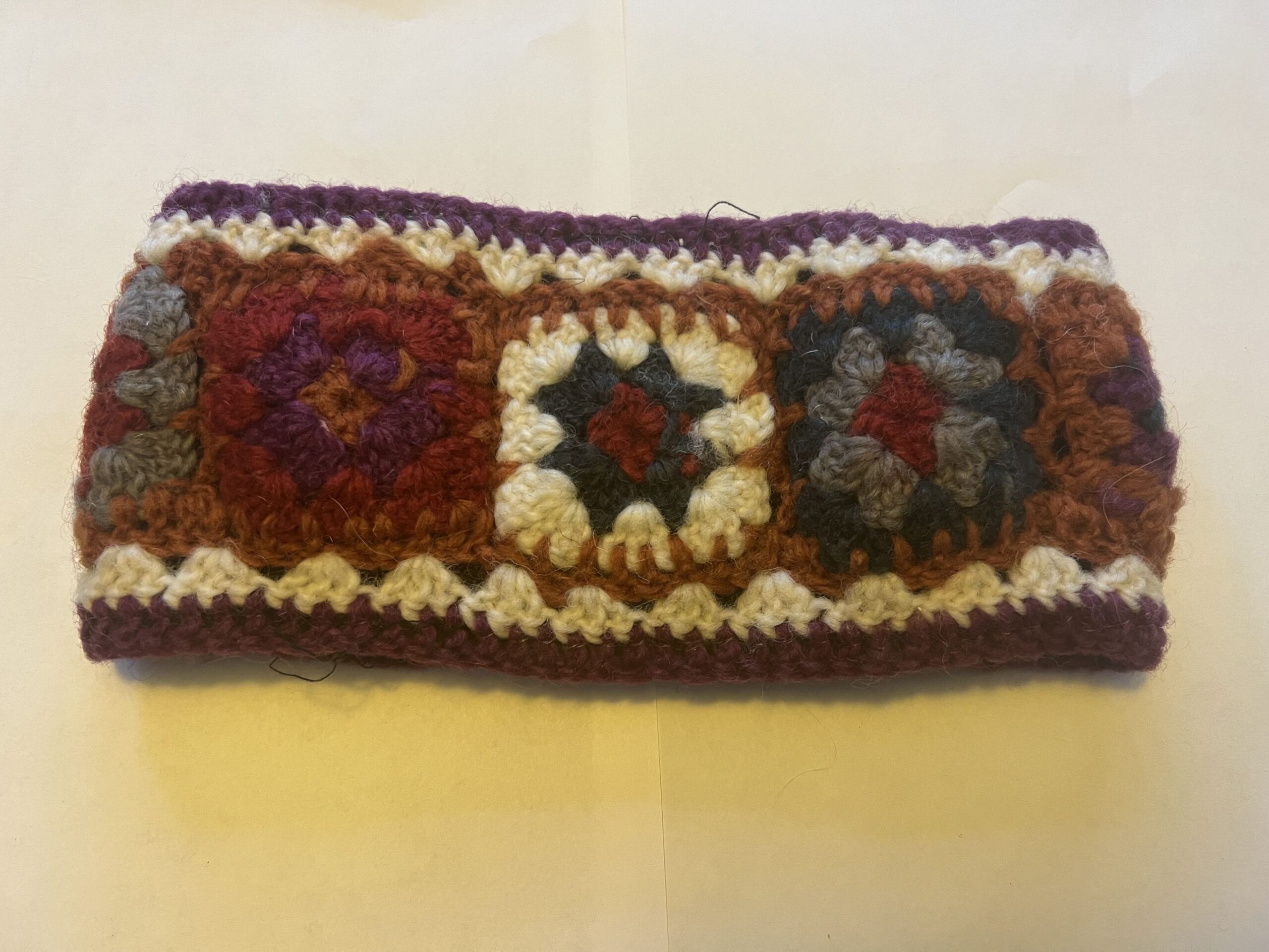 A knitted headband with flowers across the middle in white, green, red, purple, orange, and green. Made with yak wool. 