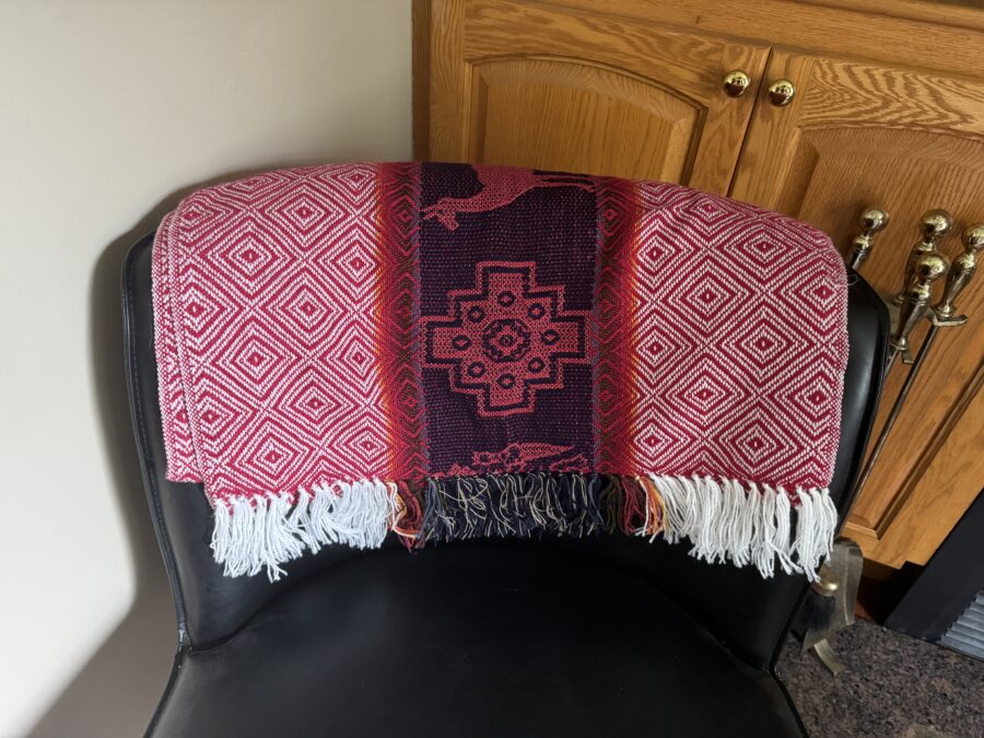 A pink and purple blanket on the back of a chair with a chakana on it