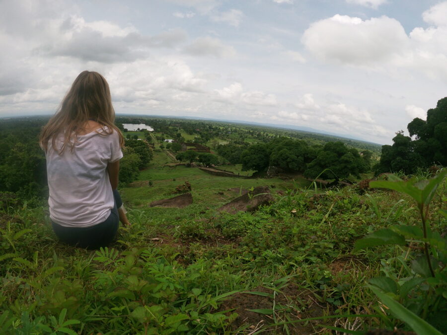 A girl facing away from the camera sitting in a field in Laos, admiring the views.