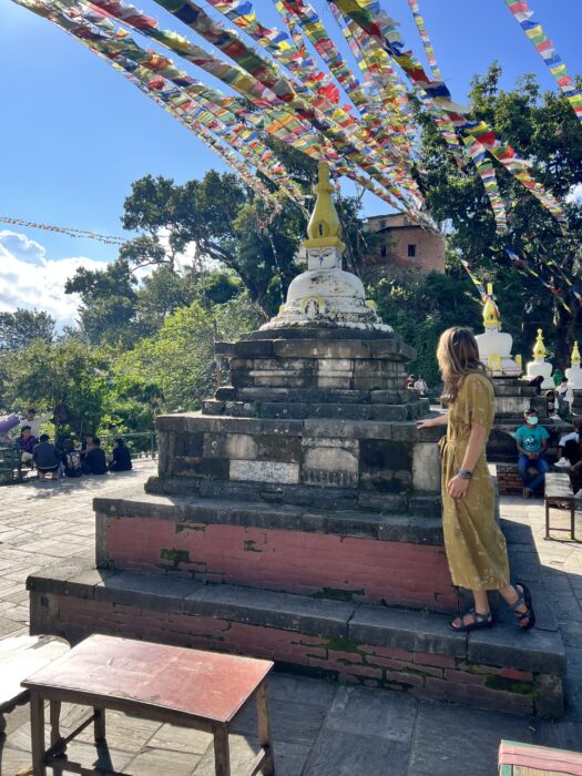 A girl in a brown dress standing under prayer flags in Nepal.